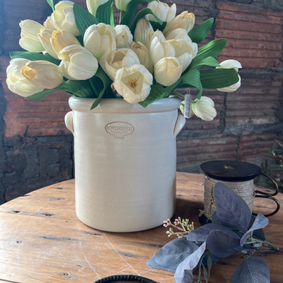                             hand thrown 2 gallon stoneware crock in a matte white finish filled with faux white tulips pictured with a rustic brick background