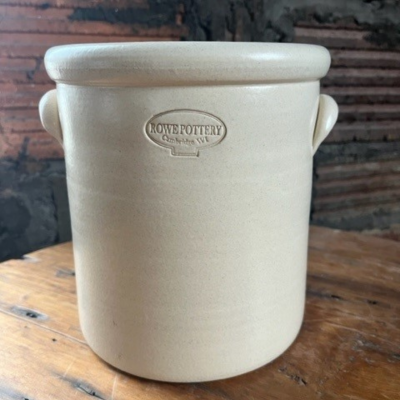        hand thrown 1 gallon stoneware crock with a Rowe Pottery branded stamp on the top of the crock, pictured with a rustic brick background                     